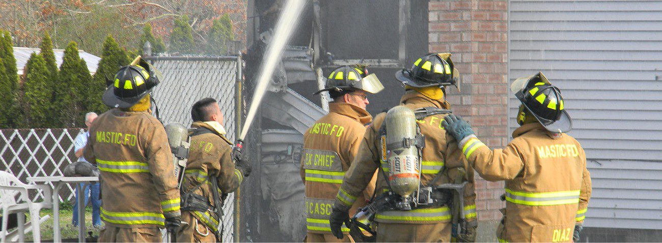 group of 8 fire fighters using a fire hose to cool a smoldering house after a fire