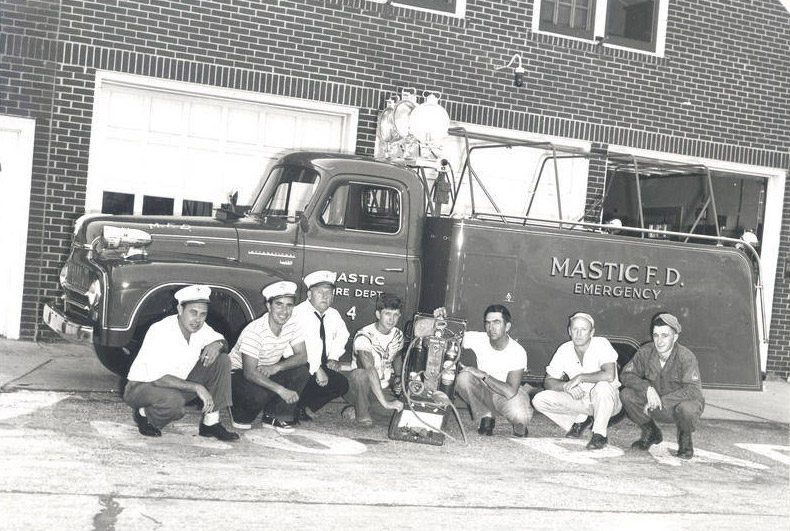 Vintage photo of firefighters sitting on and in front of a fire truck in the 1950s