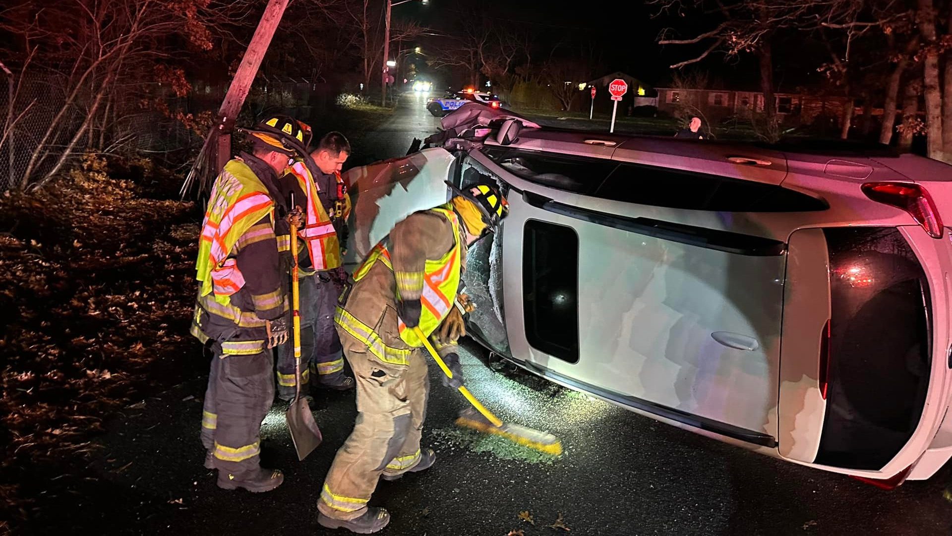 3 firefighters cleaning debris off the road at the scene of a car accident at night