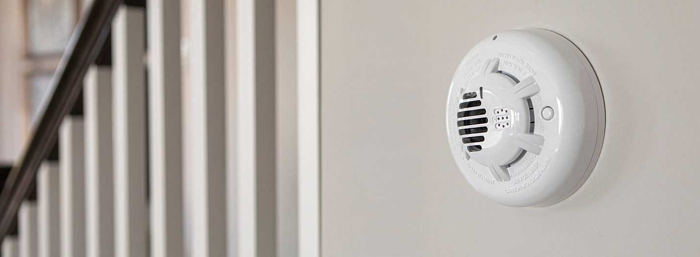 carbon monoxide detector mounted to a wall next to a staircase in a home
