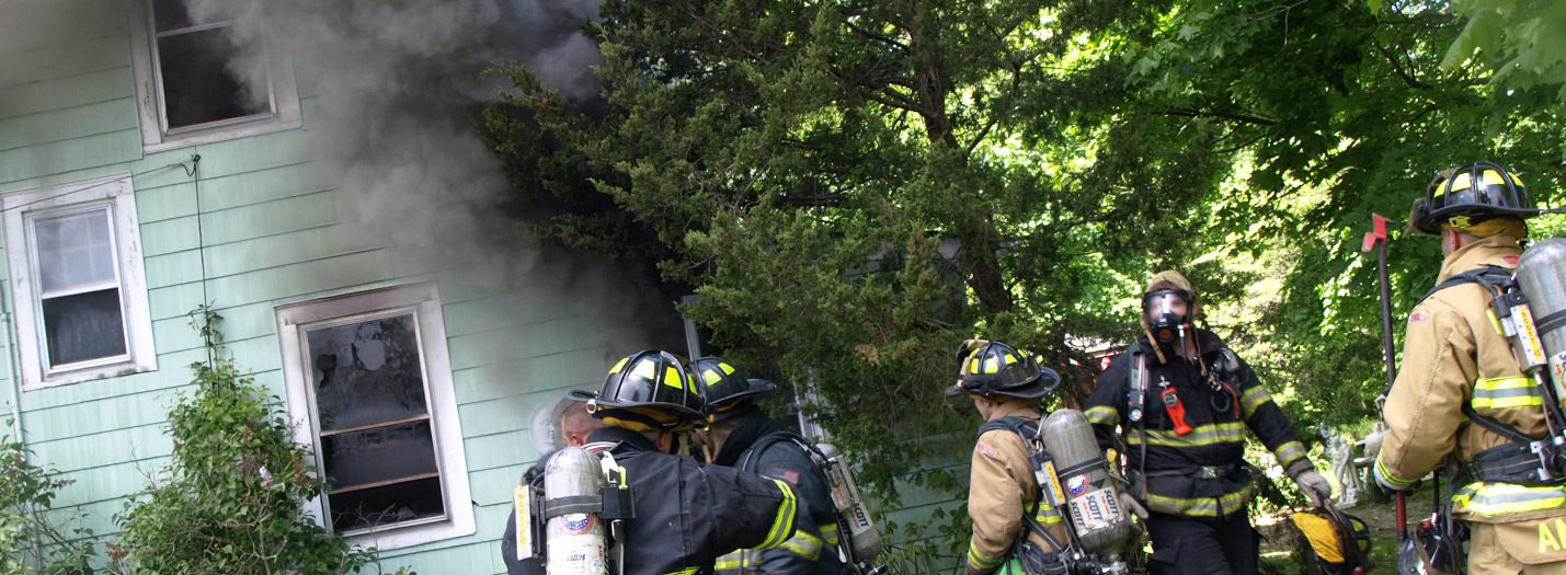Group of 6 firefighters outside of a home that has dark smoke billowing out