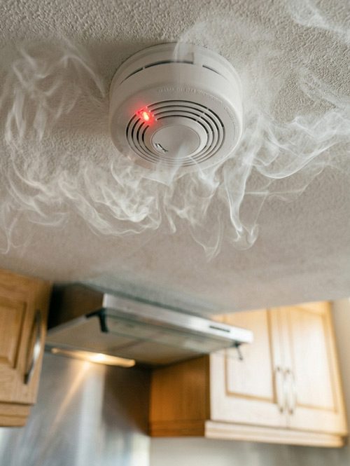 Smoke swirling around a ceiling-mounted smoke detector in a kitchen